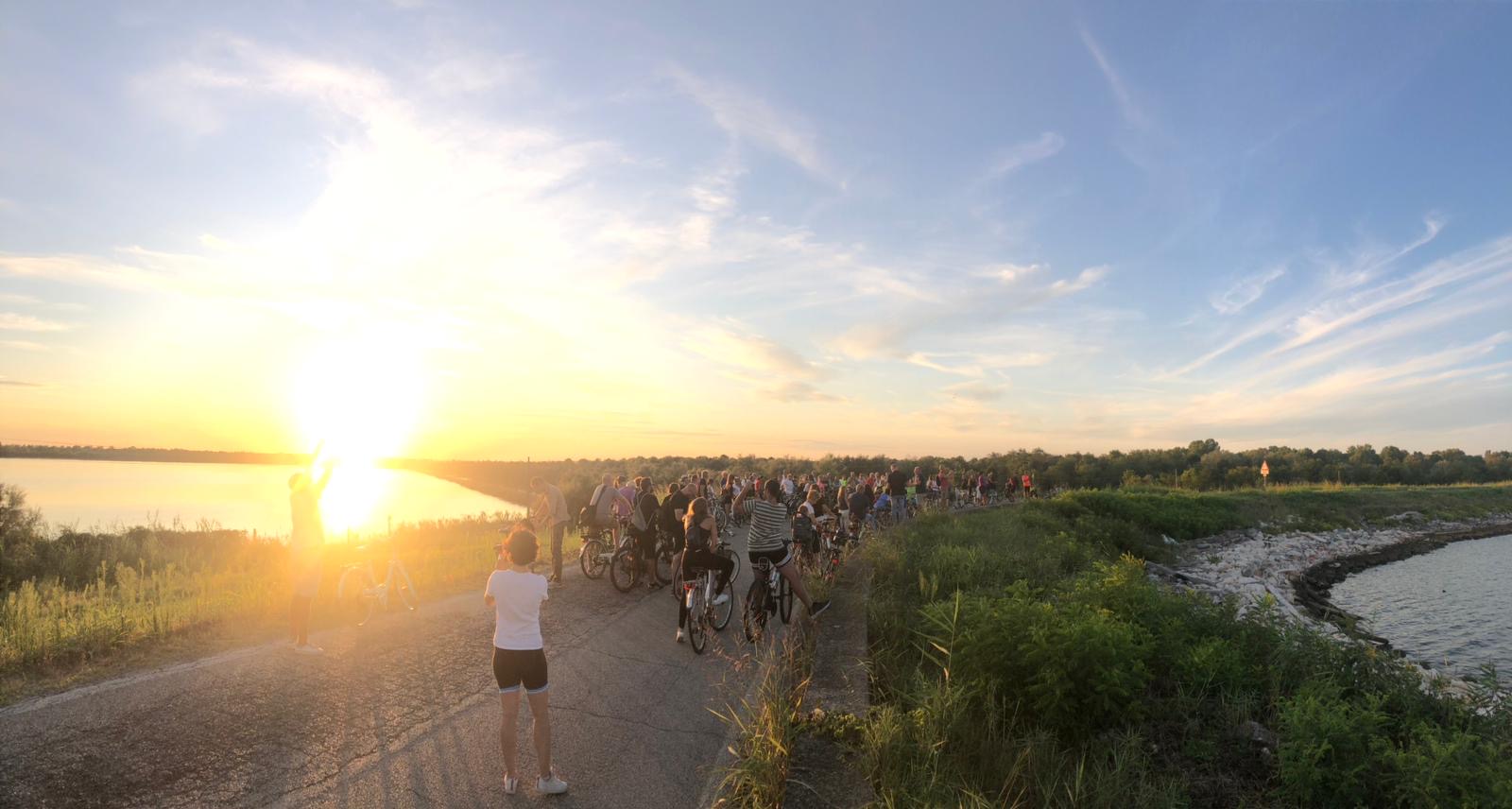 Un gruppo di persone attraversano in bicicletta il Parco del Delta del Po al tramonto