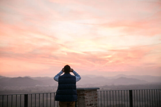 Un uomo guarda il paesaggio del Monferrato al tramonto, con un binocolo