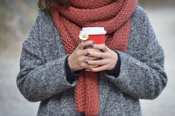 Una donna con un maglione e una sciarpa tiene in mano una tazza di thè caldo