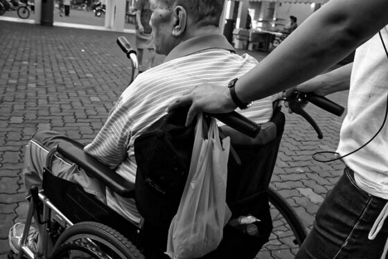 Un anziano sulla sedia a rotelle, portato da un badante 