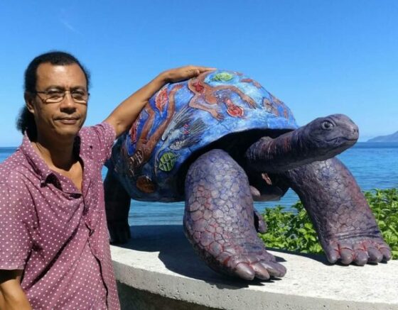 George Camille insieme ad una sua opera, una scultura a forma di tartaruga 